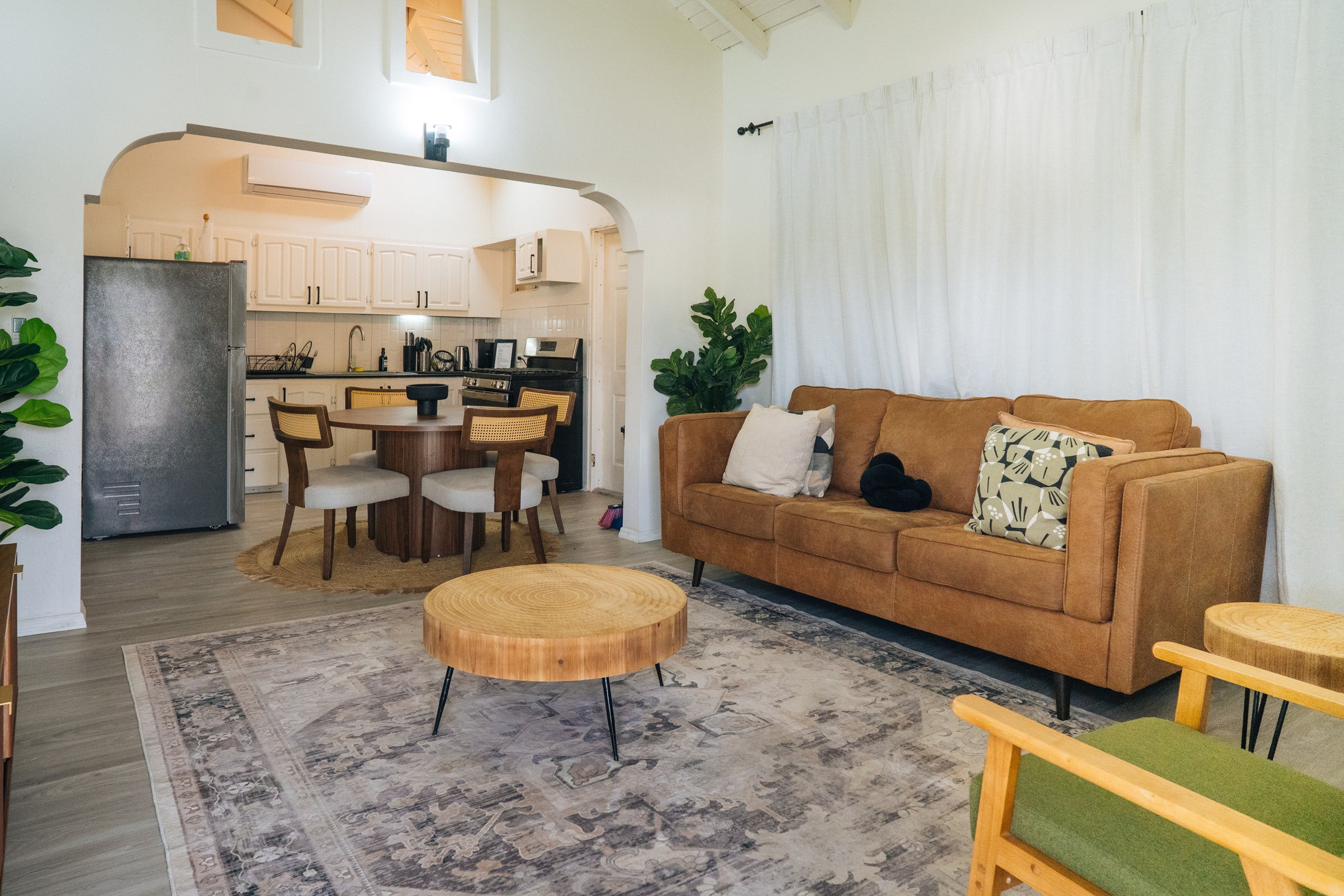 Open living room with a caramel sofa, natural wood furniture, and an adjoining kitchen